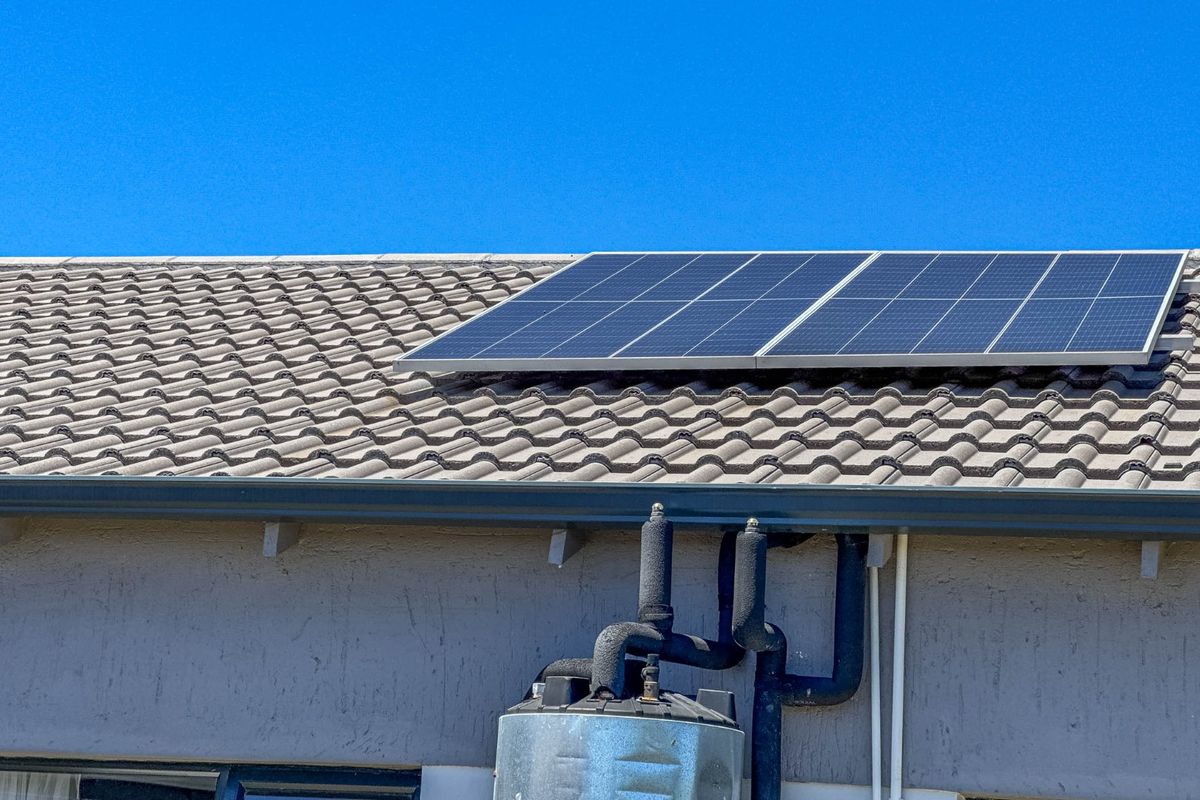 Exterior view of the roof featuring installed solar panels, guttering, and an external geyser unit with insulated piping.