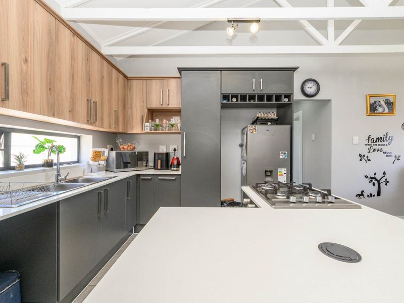 Modern kitchen featuring two-tone cabinetry, stone countertops, a gas hob, and exposed white roof trusses, creating a bright and functional culinary space.