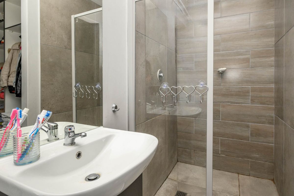 A modern bathroom featuring a ceramic basin with chrome mixer tap and a walk-in shower with glass screen and neutral wall tiling.