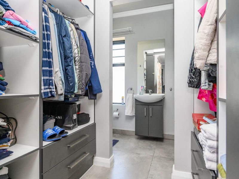 A walk-in closet area featuring built-in cabinetry and drawers, leading directly into an en-suite bathroom with a modern vanity basin.