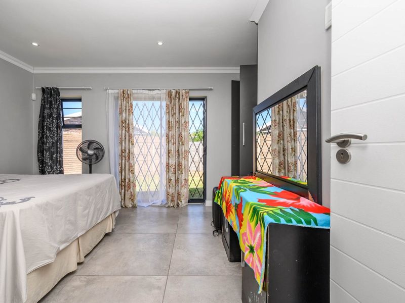 A well-maintained bedroom featuring large format floor tiles, recessed lighting, and a sliding glass door providing direct access to the garden.