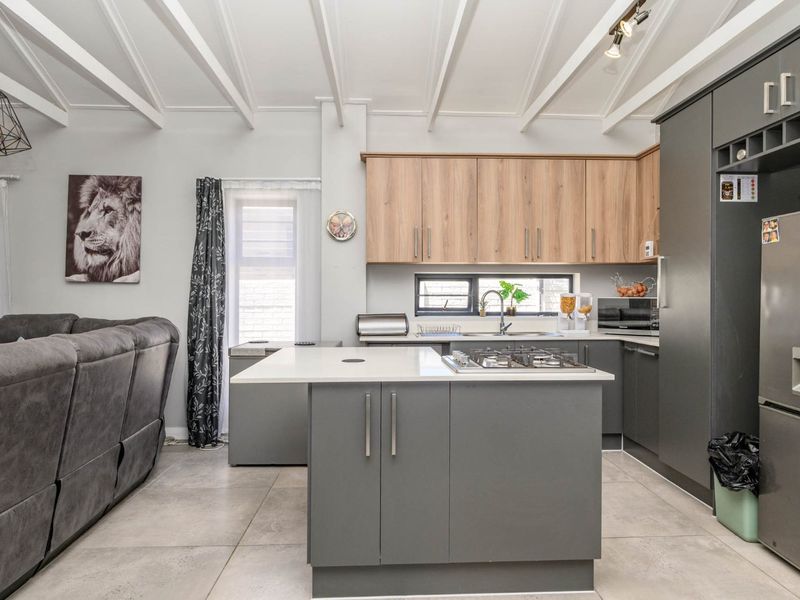 Modern open-plan kitchen featuring a central island with gas hob, sleek cabinetry, stone countertops, and exposed beam ceilings, seamlessly integrated with the living area.