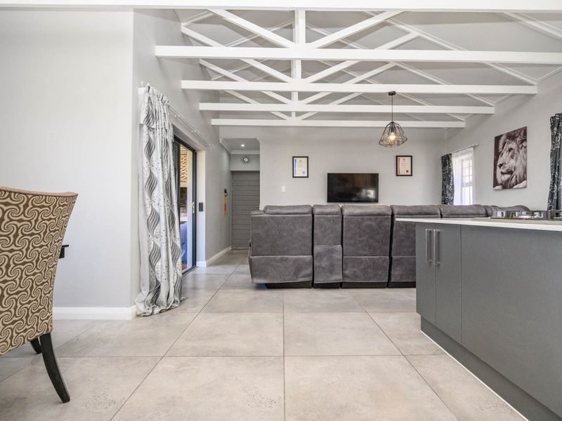 Spacious open-plan living area featuring exposed white ceiling beams, modern tiled flooring, and a functional kitchen island, creating a bright and airy atmosphere.