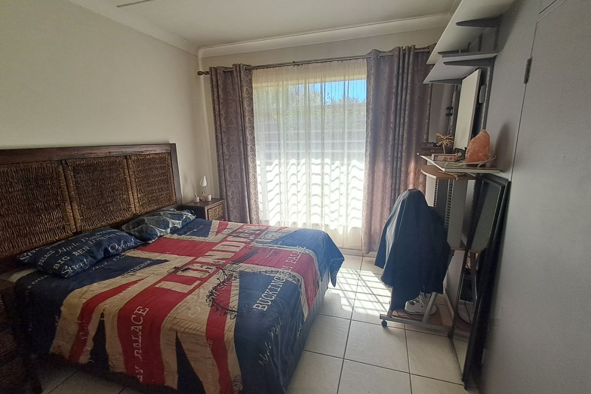 A bedroom featuring tiled flooring, built-in cupboards, and a window with curtain rails, offering a functional space with potential for modernization.
