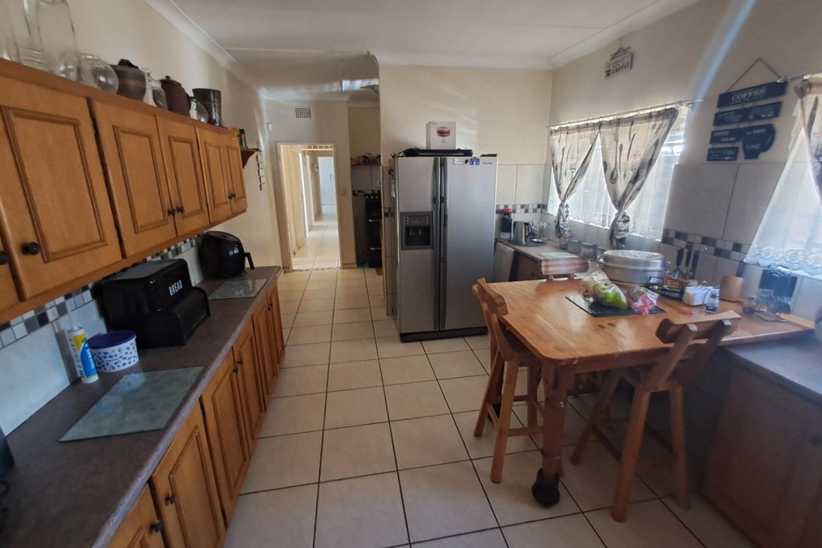 A functional kitchen featuring wooden cabinetry, tiled flooring, and a tiled backsplash, offering a practical layout with direct access to the hallway.