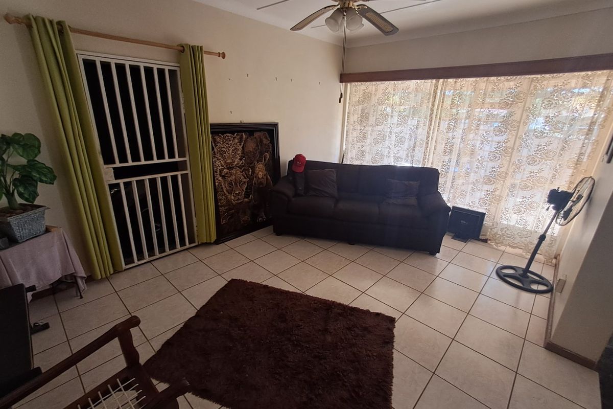 A living room featuring tiled flooring, a ceiling fan, and a security gate, offering a functional space with potential for cosmetic updates.