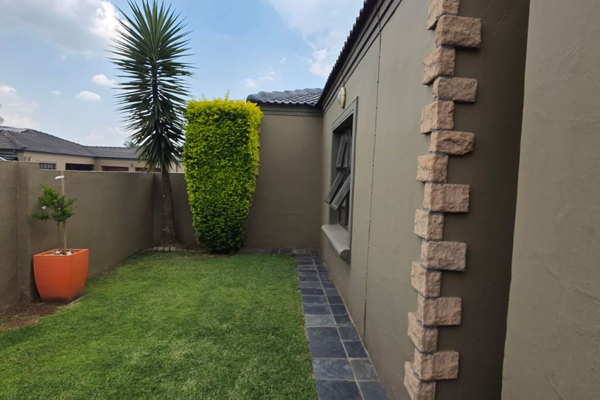 A well-maintained rear garden area featuring a neat lawn, slate pathway, and decorative stone cladding on the exterior wall.