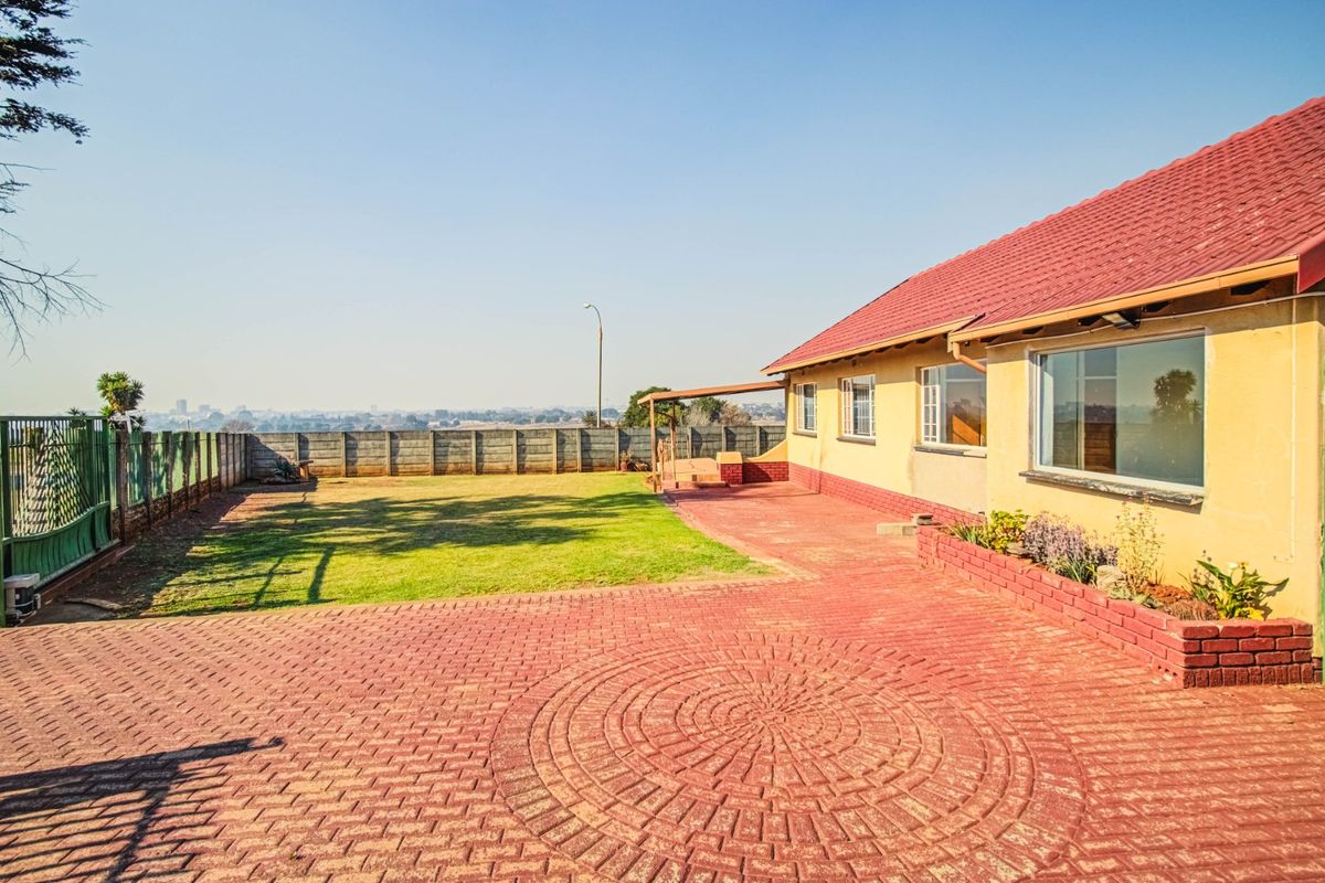 Spacious rear exterior featuring a large paved patio area, a well-maintained lawn, and a perimeter boundary wall with distant city views.
