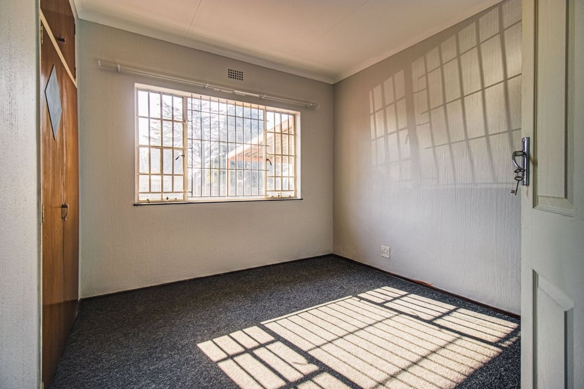 A clean, empty bedroom featuring built-in cupboards, carpeted flooring, and security bars on the window, providing a neutral space ready for personalization.
