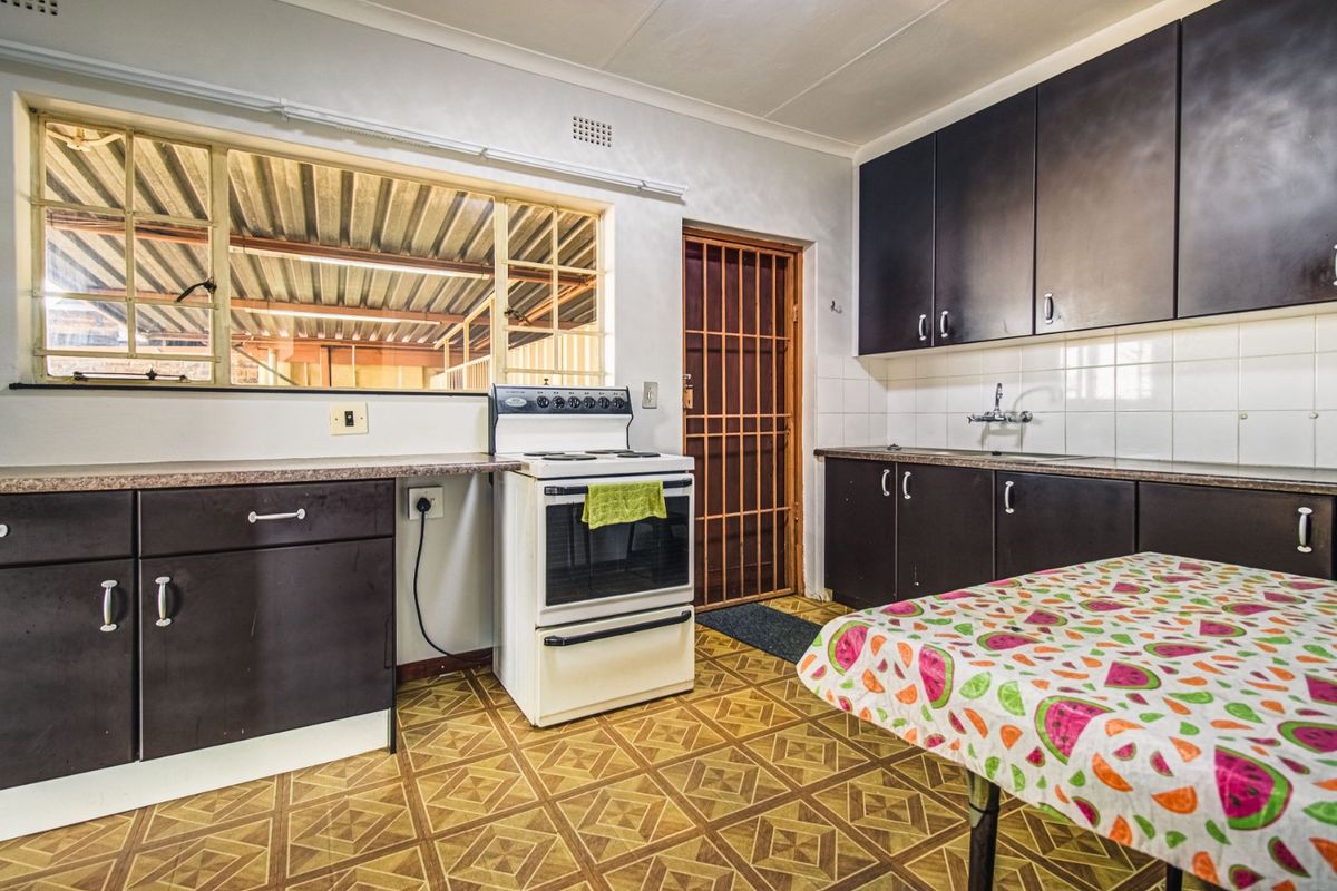 A functional kitchen featuring dark cabinetry, laminate countertops, a freestanding stove, and a security gate leading to an exterior area.