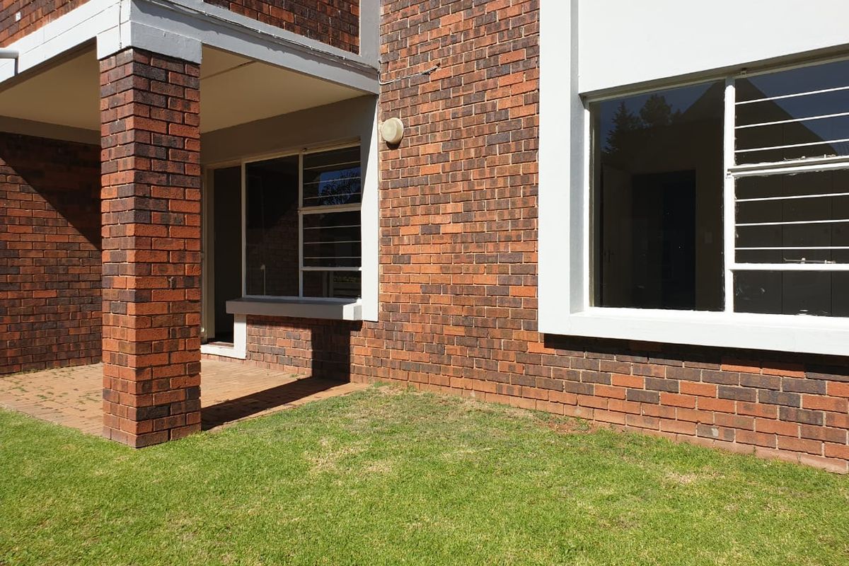 Rear view of the townhouse featuring a brick facade, a small paved patio area, and a private lawn.