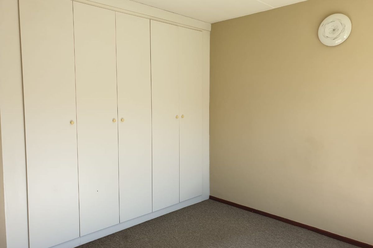 A clean, empty bedroom featuring neutral wall tones, fitted built-in cupboards, and carpeted flooring, offering a blank canvas for personalization.