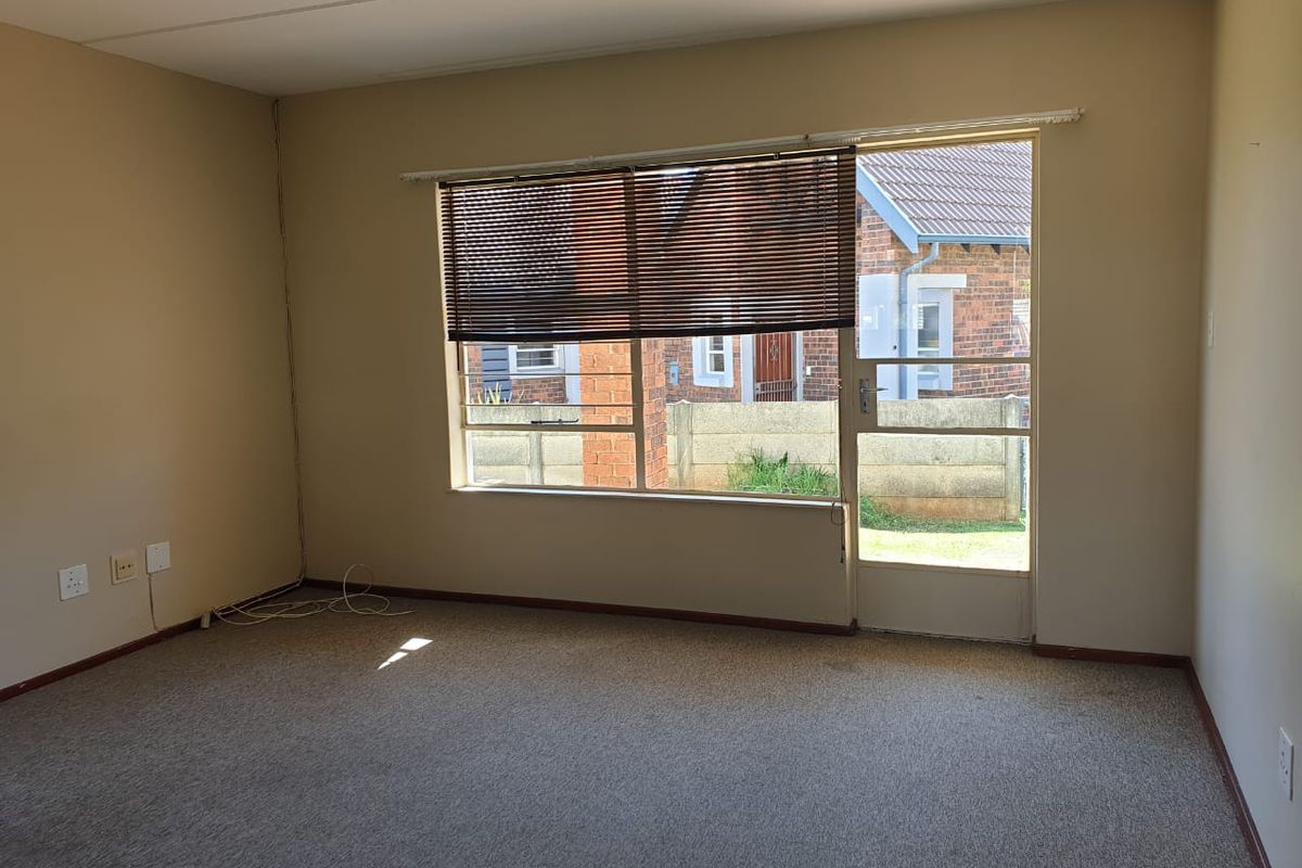 An empty living room featuring carpet flooring, a large window with venetian blinds, and a glass panel door leading to the exterior.