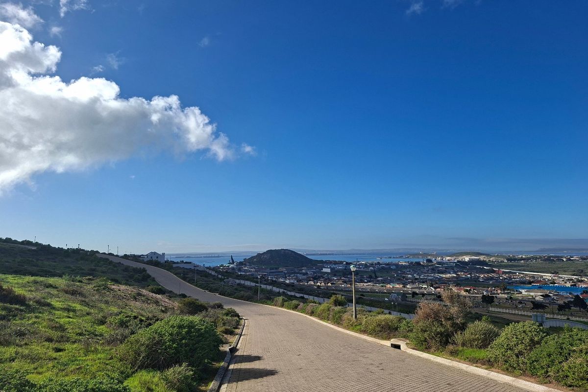 A scenic view overlooking the surrounding landscape, coastal area, and residential neighborhood from an elevated paved road.