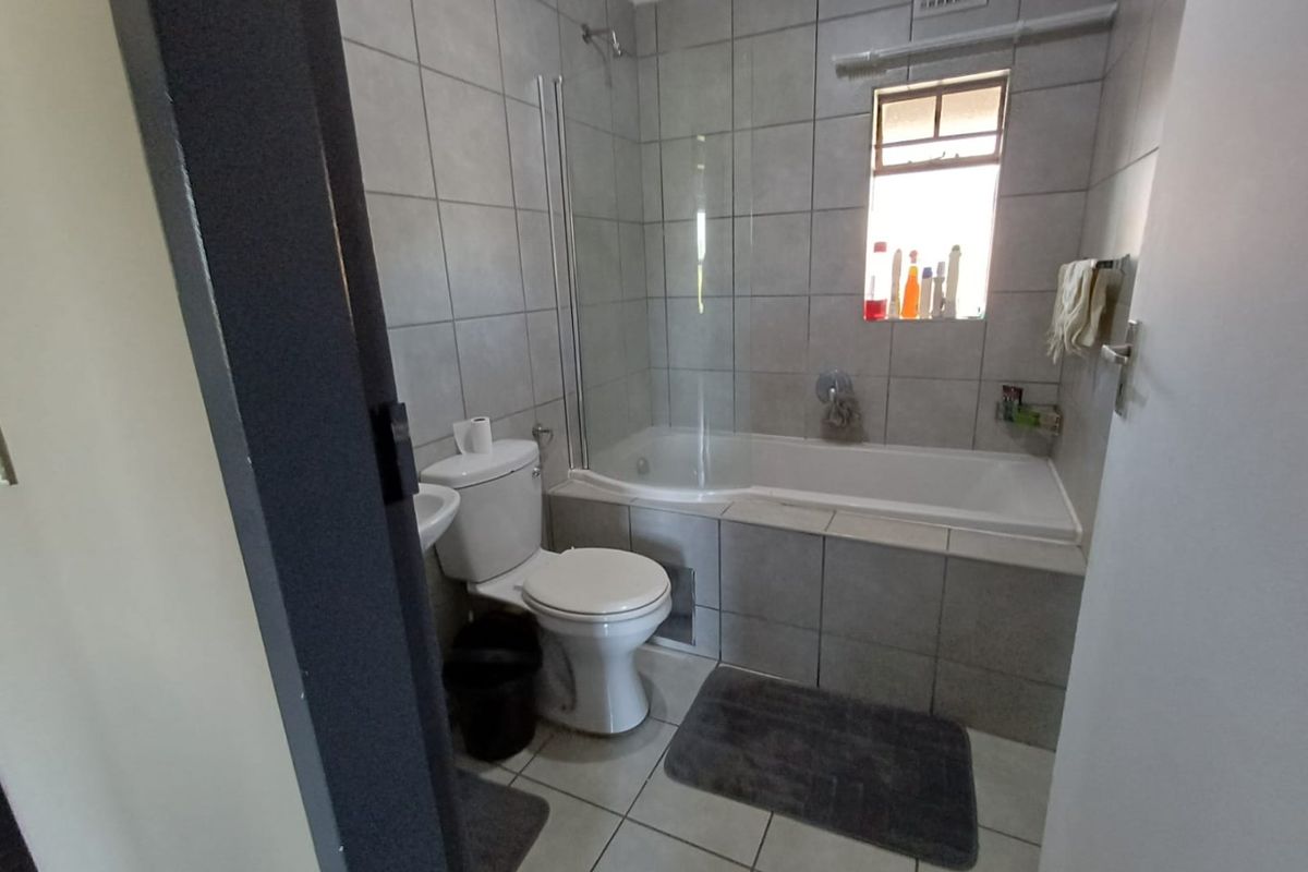 A functional bathroom featuring a tiled bathtub with a glass shower screen, a standard toilet, and neutral wall and floor tiling.