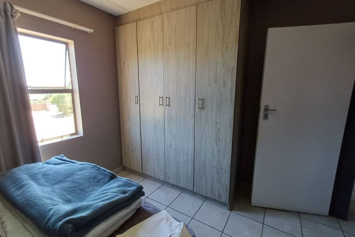 A bedroom featuring built-in wooden cupboards, tiled flooring, and a window providing natural light.