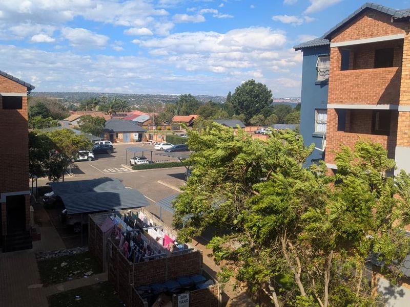 Elevated view overlooking the apartment complex grounds, featuring brick buildings, paved parking areas, and surrounding neighborhood landscape.