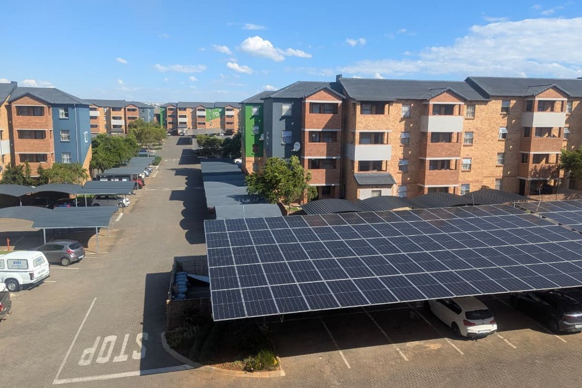 Aerial view of an apartment complex featuring multiple residential blocks, paved parking areas, and a large solar panel carport installation.