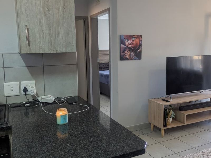 Open plan living area featuring a kitchen with granite countertops and electric hob, seamlessly flowing into the adjacent living space and bedroom access.