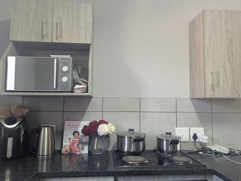 A functional kitchen area featuring modern wood-look cabinetry, a dark granite countertop, and a built-in electric hob with a tiled backsplash.