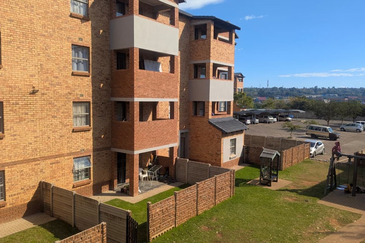 Exterior view of a multi-story apartment complex featuring face brick construction, private balconies, and shared garden space with paved walkways.