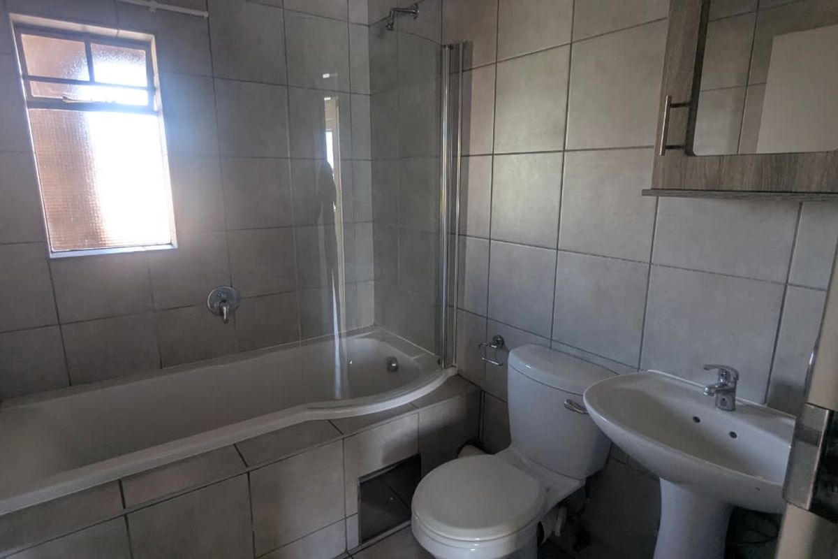 A functional bathroom featuring a tiled bathtub with a glass shower screen, a pedestal basin, and a standard toilet.