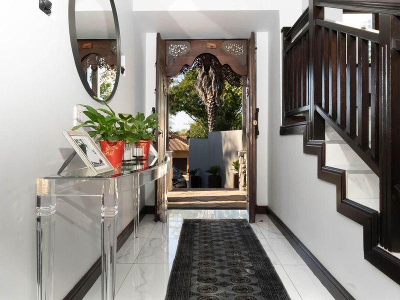 Welcoming entrance hall featuring polished marble-look flooring, an ornate timber front door, and a classic staircase with a dark timber balustrade.