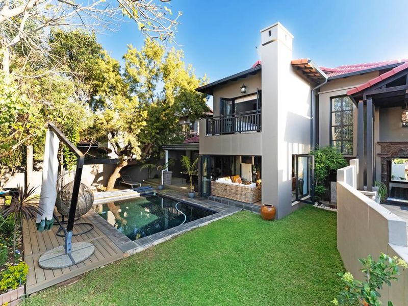 Rear exterior view featuring a swimming pool, timber decking, landscaped garden, and a two-story home with a balcony and bi-fold doors.