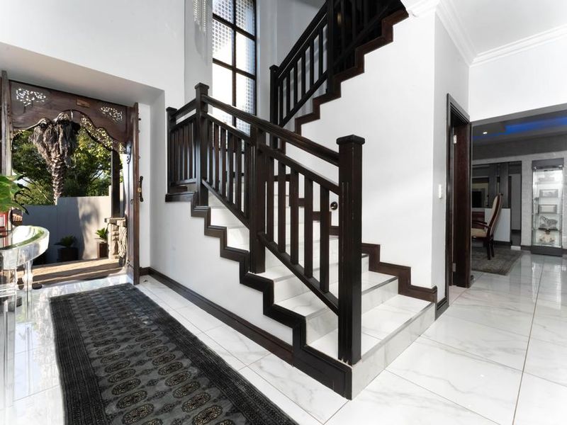 Grand entrance hall featuring a striking dark wood staircase, polished marble-look floor tiles, and an ornate carved wooden doorway leading to the exterior.