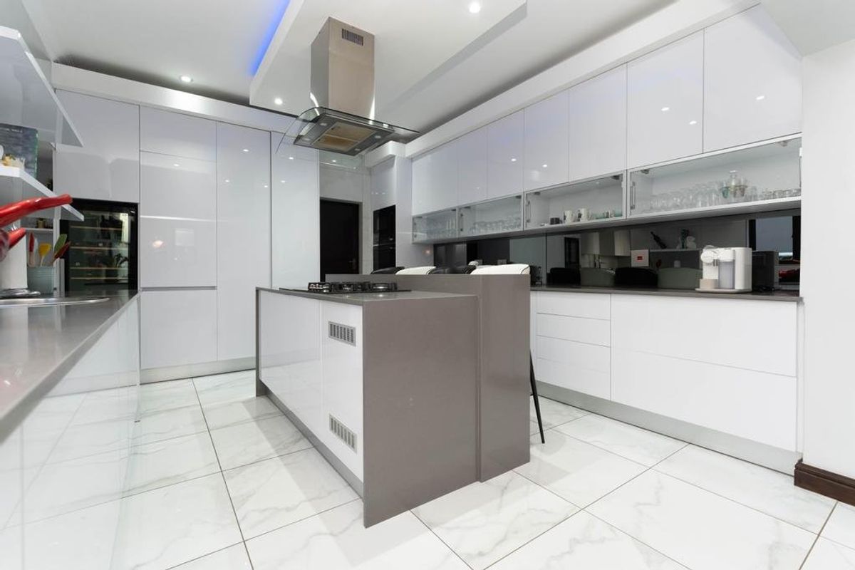 Modern kitchen featuring high-gloss white cabinetry, a central island with a gas hob, integrated appliances, and polished marble-look floor tiles.