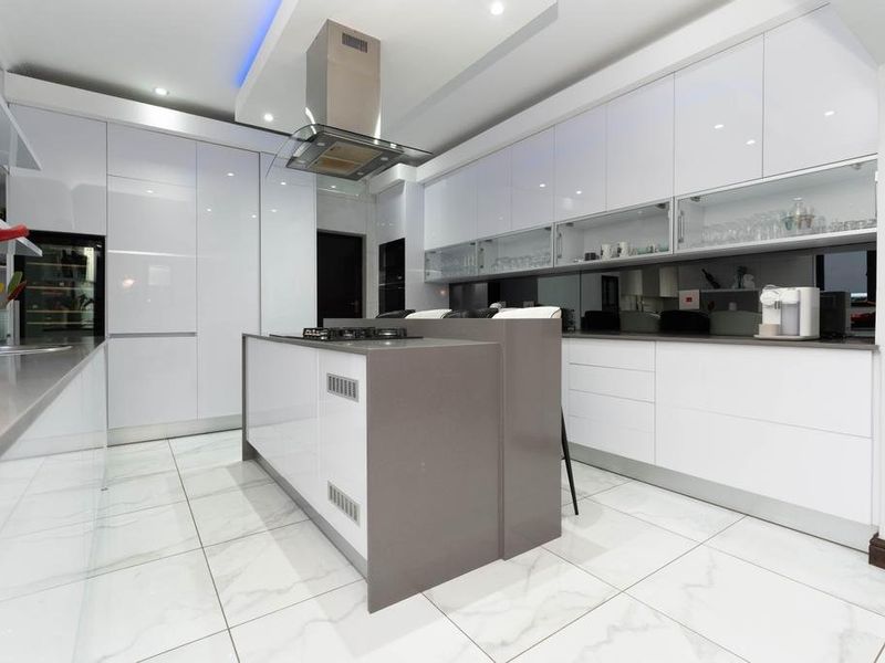 Modern kitchen featuring high-gloss white cabinetry, a central island with a gas hob, integrated appliances, and polished marble-look floor tiles.