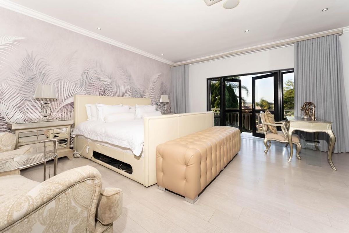 Spacious bedroom featuring light-toned laminate flooring, decorative wallpaper, recessed lighting, and double glass doors providing access to an outdoor balcony.
