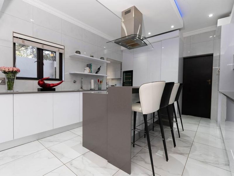 Modern kitchen featuring high-gloss cabinetry, stone countertops, integrated appliances, and a central island with breakfast bar seating.