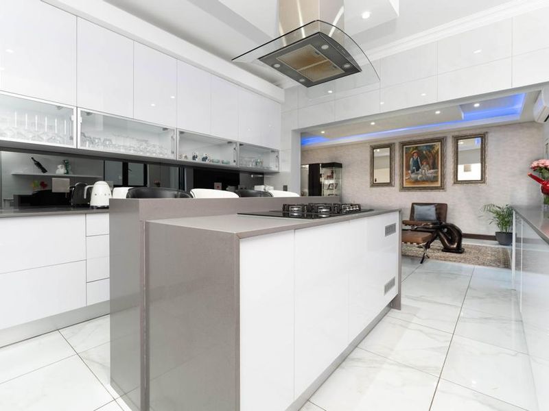 Modern open-plan kitchen featuring a central island with gas cooktop, sleek white cabinetry, stone countertops, and elegant recessed lighting throughout the space.