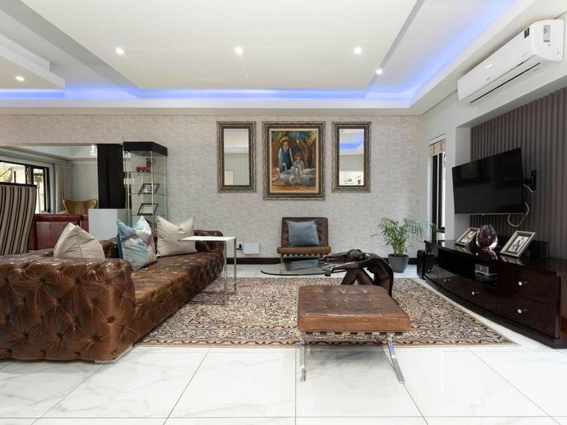 A modern, well-maintained living room featuring polished tiled floors, recessed ceiling lighting with blue LED accents, and a feature wall with slatted paneling.