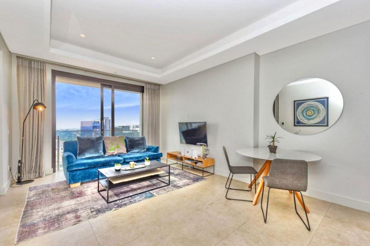 Modern open-plan living area featuring tiled floors, recessed ceiling lighting, and large sliding glass doors leading to a balcony with city views.