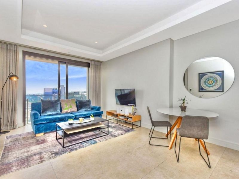 Modern open-plan living area featuring tiled floors, recessed ceiling lighting, and large sliding glass doors leading to a balcony with city views.