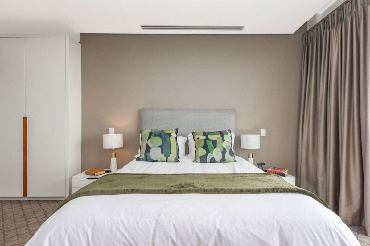 A well-maintained bedroom featuring a built-in wardrobe, neutral wall tones, and integrated ducted air conditioning.