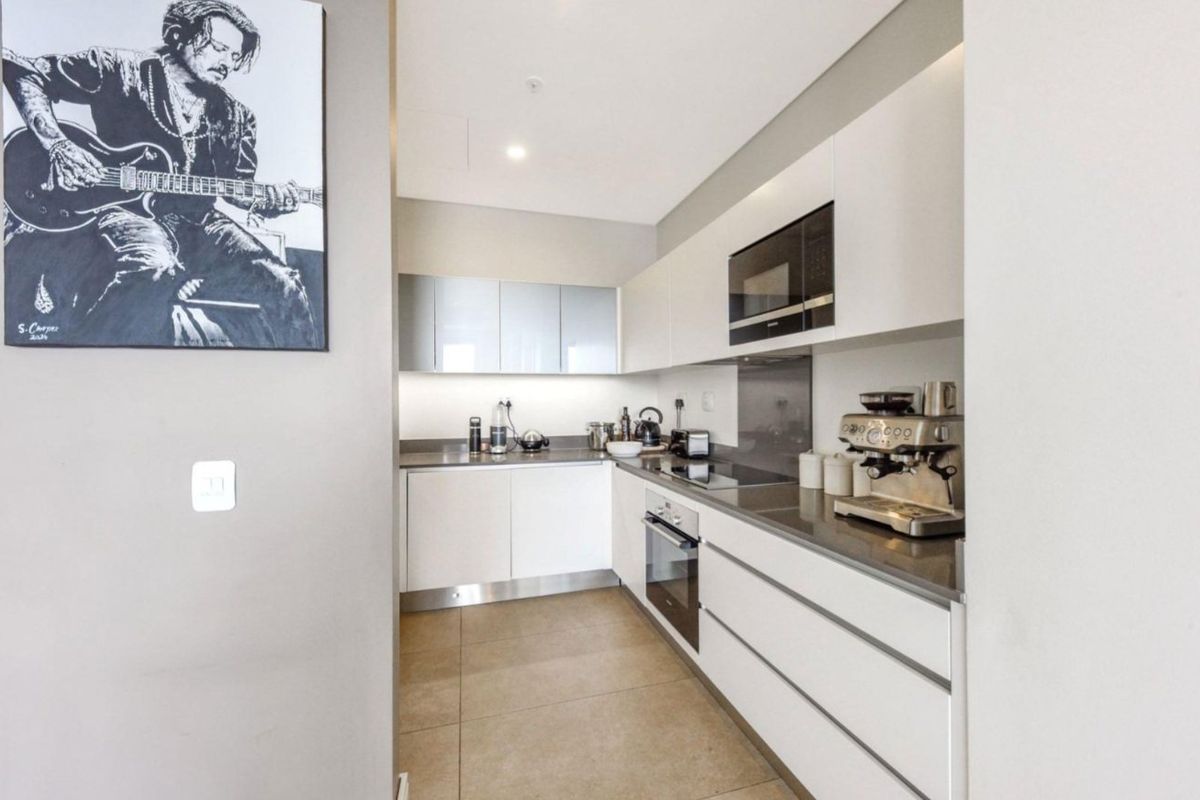 Modern galley-style kitchen featuring sleek white cabinetry, stone countertops, integrated appliances, and high-quality tiled flooring.