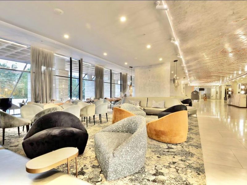 A spacious, modern lounge area featuring floor-to-ceiling windows, polished marble flooring, and sophisticated recessed and track lighting throughout the open-plan space.