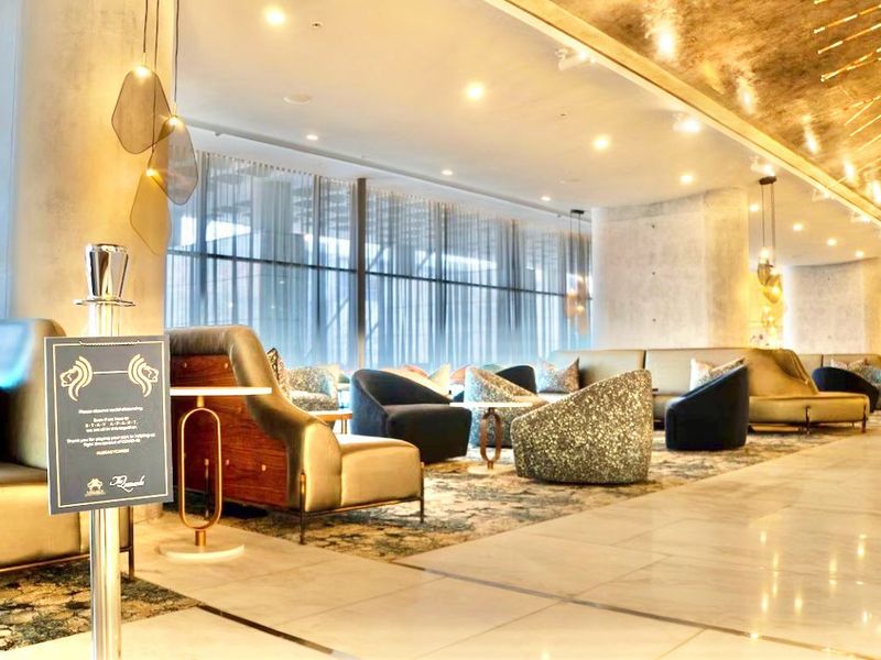 A modern, upscale lounge area featuring polished marble floors, floor-to-ceiling windows with sheer curtains, and contemporary recessed ceiling lighting.