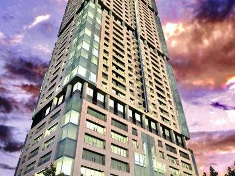 A low-angle view of a modern high-rise apartment building featuring a glass and concrete facade against a sunset sky.