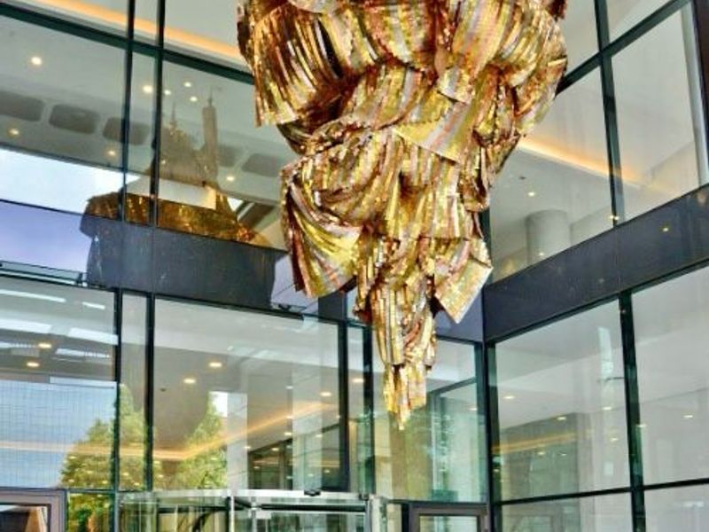 Modern apartment building entrance lobby featuring a full-height glass facade, revolving glass doors, and a prominent decorative gold pendant light fixture.