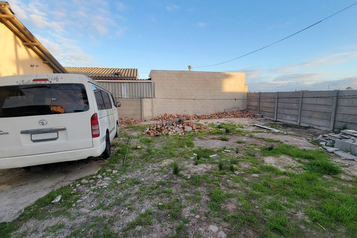 A rear exterior area featuring a concrete boundary wall and an unlandscaped yard with visible construction debris and rubble.