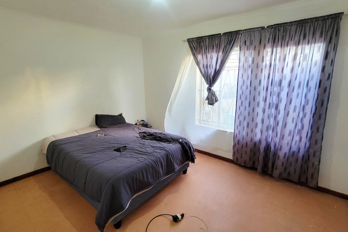 A bedroom featuring a window with security bars and basic flooring, offering a functional space ready for updates.