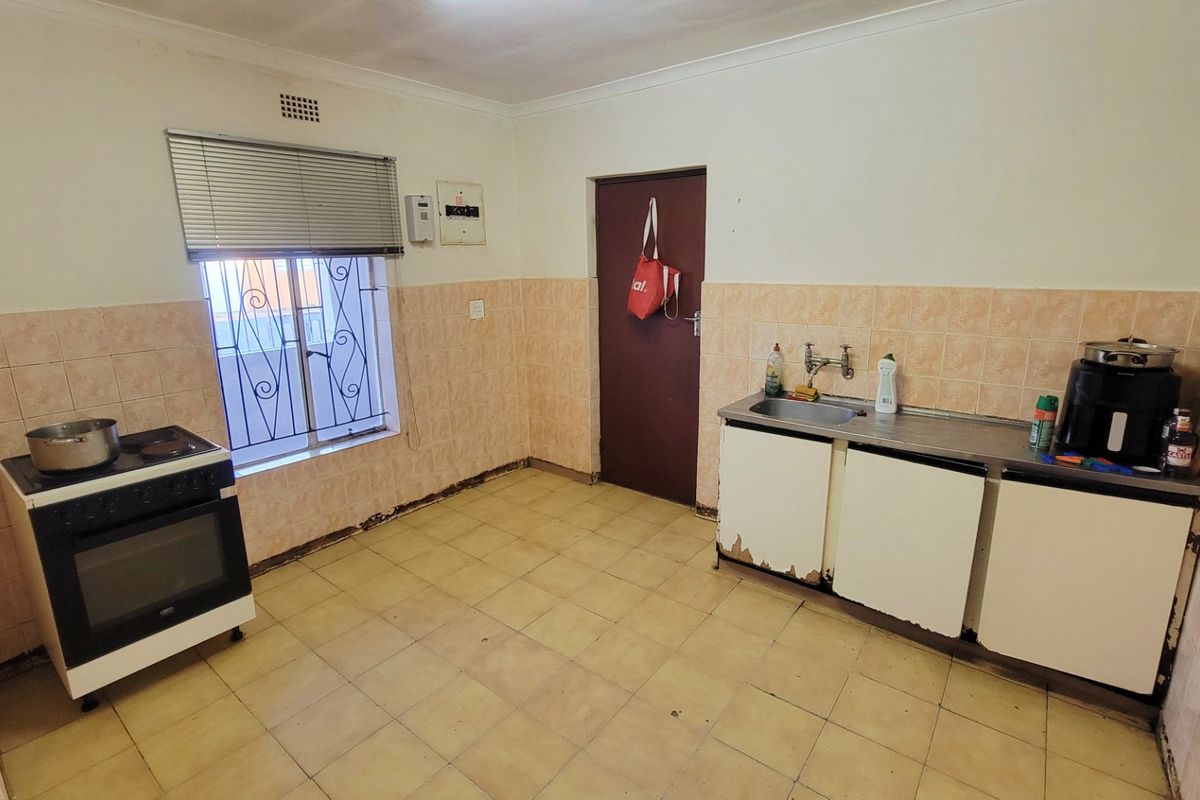 A dated kitchen featuring tiled walls, a stainless steel sink, and a freestanding stove, requiring cosmetic updates and cabinetry repairs.