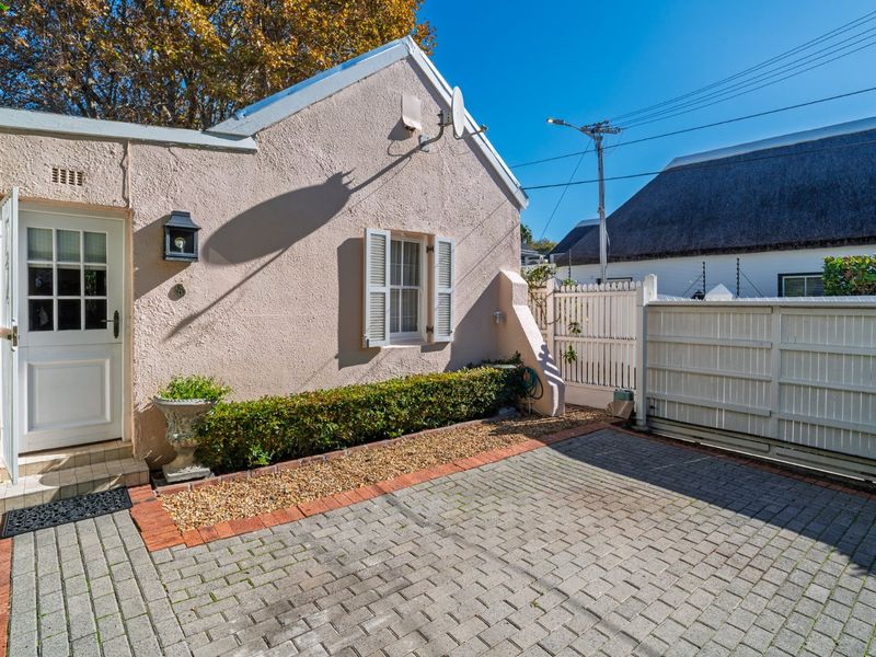 A well-maintained front exterior featuring a paved driveway, brick edging, a charming shuttered window, and a secure gated entrance.