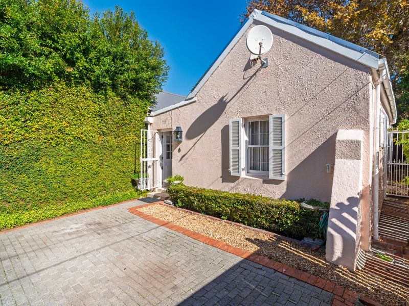 A well-maintained front exterior featuring a paved driveway, established hedging, and a charming facade with shuttered windows and secure entrance.