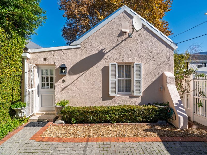 Charming front facade of a cottage-style home featuring a paved driveway, textured exterior walls, shuttered windows, and a secure gated entrance.