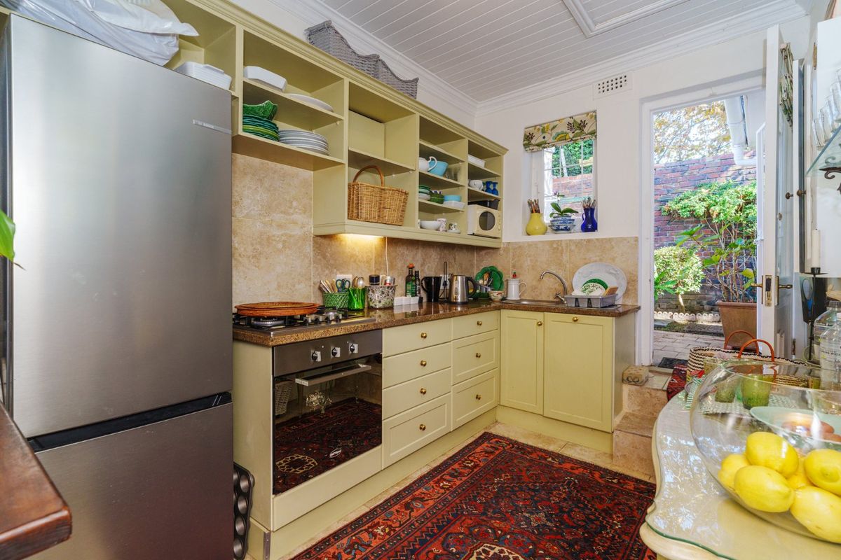 A compact kitchen featuring light-toned cabinetry, stone countertops, built-in oven and hob, and direct access to a rear garden area.
